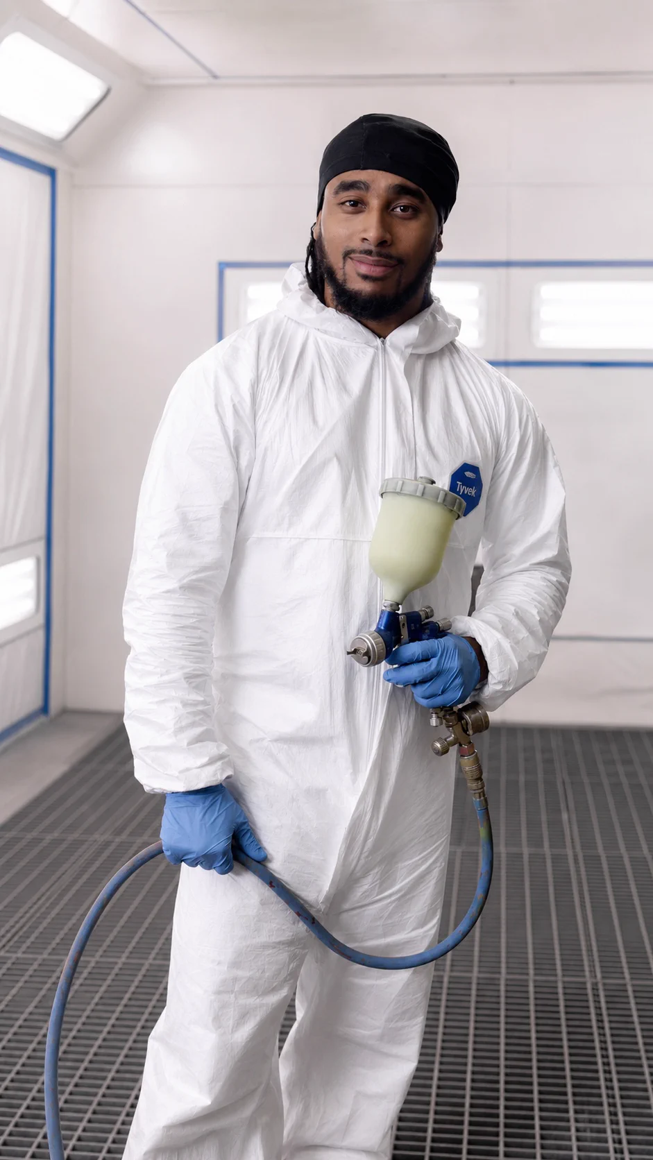 Jay in a professional spray booth, white Tyvek suit, holding HVLP gun